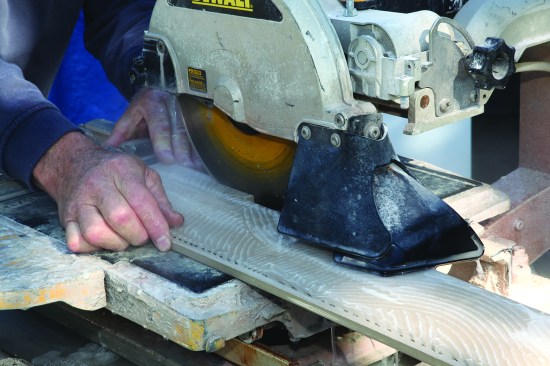 He flips the tile over, and finished the cuts from the back.