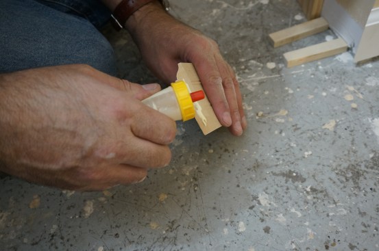 Before installing the mating piece at the corner, the author apples carpenter's glue to the joint. Note in the background spacer blocks are in place to hold the piece at the right height for the flooring.