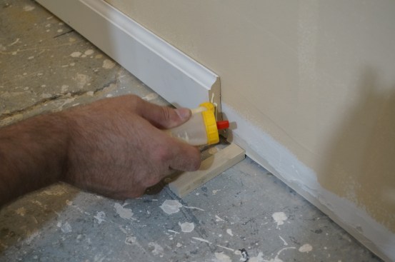 To install a length of baseboard with a scarf joint, set the first piece on the sapce blocks and apply glue to the joint.