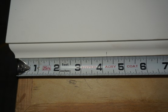 To make an accurate measurement from the short point of an angle for an outside corner, align the short point with the edge of the work bench or saw table, and hook the tape on the table to pull the measurement.