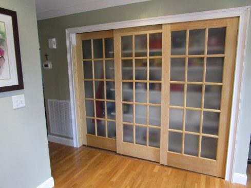 To install each bypass door panel, the author first slips the bottom guide pins into the track. Then he lifts one side of the door at a time to engage the door hardware with the roller pins.