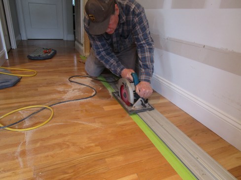 In order to mount the bottom guide tracks flush with the floor, the author carefully cut out a section of the hardwood flooring using a track saw.
