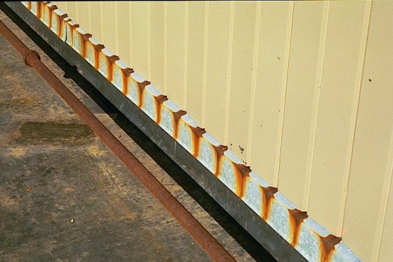 Painted metal siding panels in contact with galvanized metal flashing provides a good example of how dissimilar metals can react. The coating on the vertical panels provides protection to a point, but the differential movement of the siding panels has worn that coating off at every joint. In the presence of water, the exposed metal of the siding has reacted with the more active galvanizing on the flashing, creating a pattern of rust spots on the flashing.