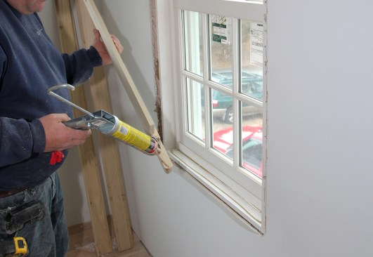 This carpenter opted to apply adhesive to the backside of the stool where it fit against the window and the drywall. Many carpenters skip this step to make the stool easy to remove in the future.