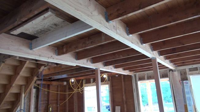 After leveling the first floor, the crew installed new LVL carrying beams along the long dimension of the house (from front to back). The existing floor was framed with 26-foot 2x7 sawn floor joists, spanning the entire width of the house. Over a century in service, and supported only by light board partitions, the floor had sagged more than four inches. The crew cut the existing full span roughly into thirds, installed engineered carrying beams, jacked the floor up, and supported the new girders with Douglas fir posts.
