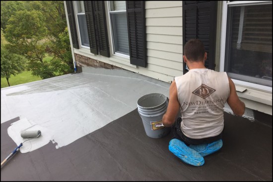 Here, a worker is applying the first of two silver-colored finish coats using a 1/2-inch nap slit foam roller and brush.