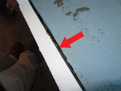 In this view from above of what should be an open drainage space (arrow) between the white EPS board and the blue substrate, it’s apparent that adhesive has filled the whole space.