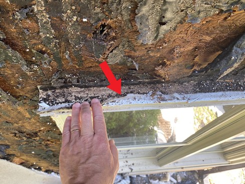 The heavy bead of sealant on top of this window head flashing blocked the drain path from the vertical channels above the window (arrow).