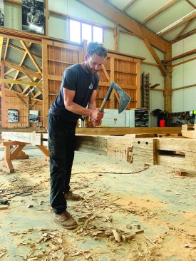 The author uses a Gothic broadaxe to hew an oak beam.