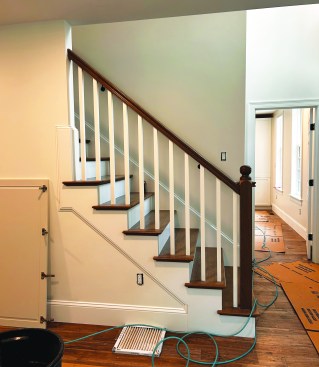 The finished stair with oak bull-nosed treads, newel post, scotia molding (under the tread nosings), handrails, and painted poplar risers, skirtboards, and balusters.