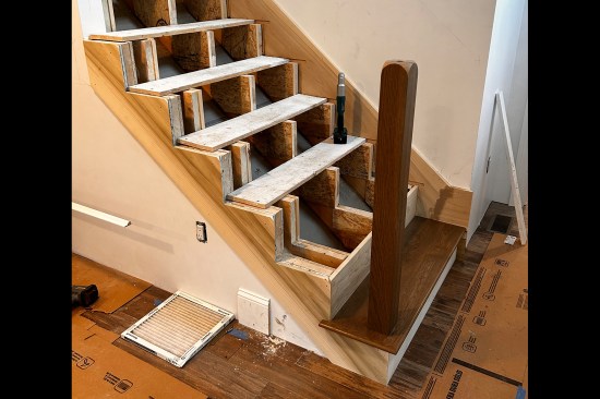 After installing the first tread, the author used a story stick to locate the underlying pocket, then used a router to cut a hole in the tread to receive the 4x4 post. The newel was glued and screwed in place.