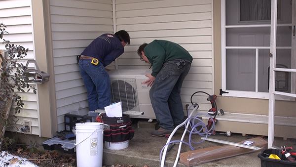 Dave Ragsdale and Chris Blaisdell set the outdoor unit of a Fujitsu Halcyon one-ton mini-split system onto masonry supports. Bolts drilled into the masonry will secure the unit in place. Typically, ReVision Energy installs the outdoor part of the heat pump onto a wall bracket or wooden stand next to the house, elevated at four feet so that the unit won’t be blocked by winter snow. But in this case, the sheltered location in the home’s rear entry alcove allows an installation close to ground level.
