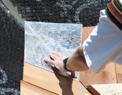 I install the first valley shingle of the starter course, nailing about 1 inch above the exposure line and 6 inches out of the valley. I use 1 3/4-inch stainless steel ring-shank nails exclusively, with the gun pressure adjusted to set the heads flush with the surface. The opposing shingle goes on next, followed by a 12-by-12-inch square step flashing, bent corner-to-corner, with its lower tip held to the butt line and nailed at the two outside corners.