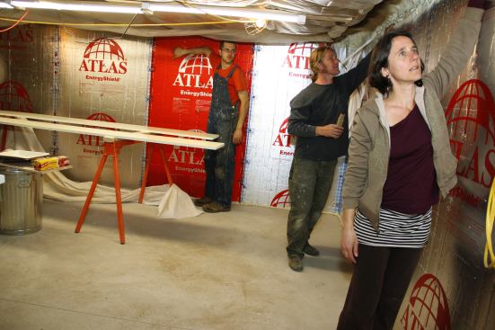 Crew members Will Markow and Dale Cunningham and architect Rachel Conly feel for air leaks at the top of the basement wall’s interior rigid insulation layer. Air intrusion at the top of this wall was noticeable during the blower door test.