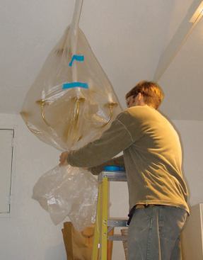 Fragile light fixtures are removed from the work area and hung from the garage framing to keep them out of harm’s way. A sheet of plastic draped over the framing and fixture and fastened with tape keeps them free of dust.