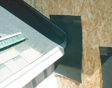 A water diverter (kick flashing) was installed by the author's crew in a retrofit job: This design will lead water out away from the wall and dump it off the roof's drip-edge rather than into the wall. Papers installed on the main wall can readily integrate with the membrane and flashing between roof and wall at the rafter tail.
