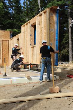 The crew eases the panel onto the slab, guiding it over a plastic plumbing pipe.