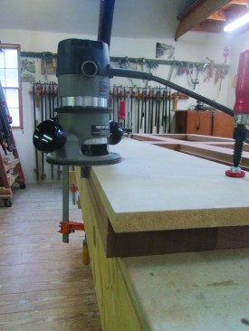 The door is too big to be cut to its finished size on a table saw. Instead, the author uses an MDF straightedge to guide a pattern bit to square the door to its final dimension.