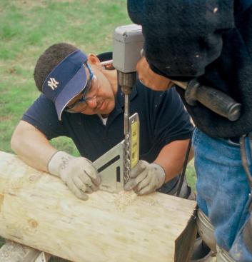 A torpedo level and a layout square are used to guide the drilling of holes for the anchor bolts.