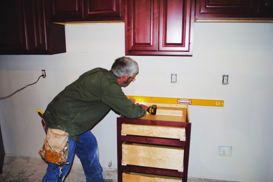 Once the base cabinets are leveled, the author secures them to the wall with screws.
