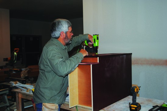 He tacks the finished face frames to the cabinet fronts.