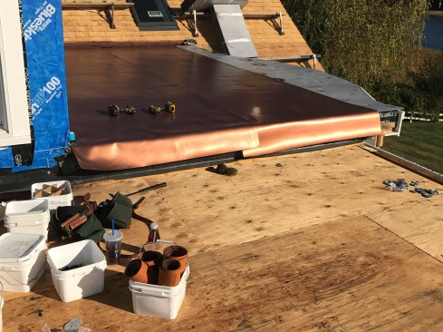 After stripping the old EPDM roofing and fiberboard underlayment, the existing deck was bloom cleaned, then rigid foam underlayment was installed. The rigid foam provides a smooth base for the PVC membrane, as well as protecting it from minor deck imperfections, such as slightly proud nail heads. When rolled out, the 60-mil Sentinel Copper Art membrane is heavy enough that it lays flat.