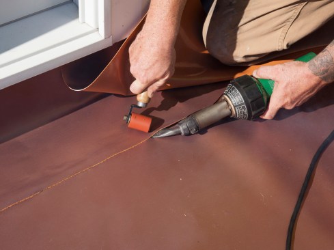 Lastly, the roof-to-wall flashing seams are welded. Here, the installer welds the horizontal leg a lapped joint. The roof-to-wall flashing’s vertical side lap and 90-degree corner are also welded—all membrane-to-membrane seams are welded with the Leister.