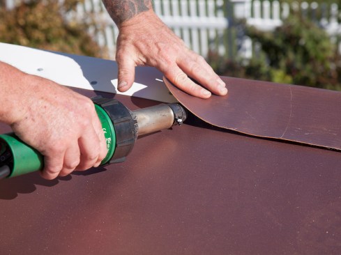 The drip edge was nailed off with stainless steel roofing nails at a rigorous 3- to 4-inch on-center spacing (replacing membrane stress plates along this edge). To finish it off, a PVC cover strip was welded down over the drip edge. 