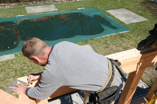 Here a crew member draws a line half the thickness of the hip stock away from the corner line. This line is used initially for measuring and then again to align the hip rafter during installation.