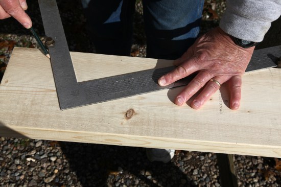 To draw a  plumb line for the cut at the top end of the hip rafter, slide the square against the edge of the rafter stock and trace along the short side of the square.