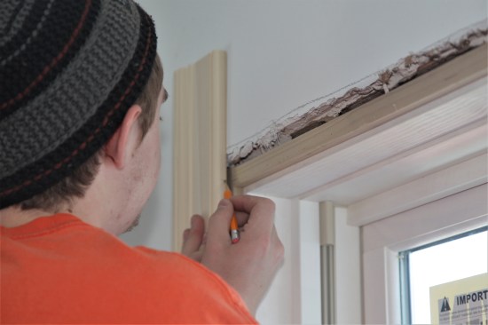 As before, he marks the length of the side casing. Note that the drywall is proud of the jamb in this corner, even with the extension strip. The carpenter will carefully break the edge of the drywall to allow the casing pieces to lay flay.