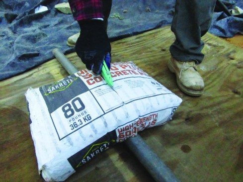 Bagged premixed concrete has many advantages and is convenient. The 80-pound bags can be arduous to handle all
at once, so the author cuts the bags in half. First, he places the bag over a pipe and slits the top paper.