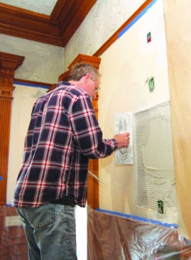Ron Bisson applies brown coat to a textured wall using a putty knife and a trowel.