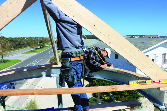 After laying out the rafters, the crew measures from the plate to the shoulder of the angled cut to find the length of each rafter.