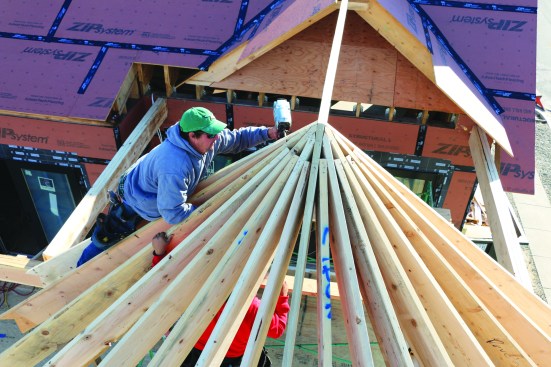 A crew member nails the tops of the rafters at the peak ...
