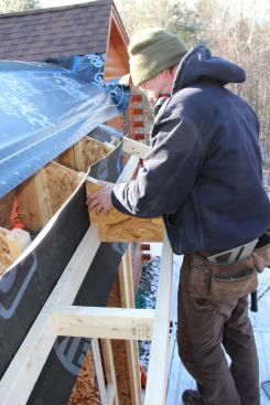 Kruse sets an OSB stiffener and nailer into place where the eave attaches to the I-joist wall buildout for the superinsulated addition.