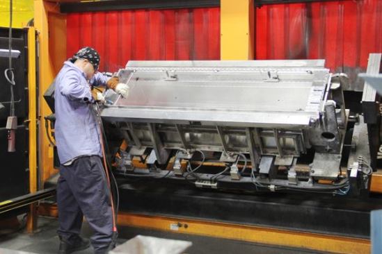 Weather Guard’s aluminium boxes are produced in a separate area of the plant. This worker has positioned the parts for a model 127 Saddle Box (a cross box) in a robotic welding fixture and is tacking pieces the robot can’t get to. It’s easier to understand if you 
watch the video.