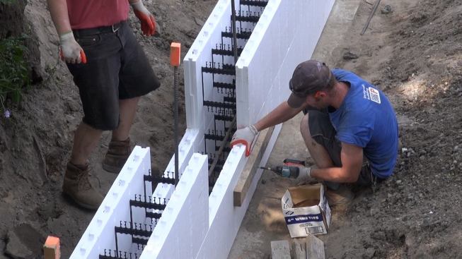 Steve Daly screws a 2x4 scab into the plastic ribs of the foam forms, to create a reinforcing scab at the point where the last segment of foam form has been cut and pieced into place. The ICF system supplier recommends making all the joints in the wall at a single point, which can then conveniently be reinforced with scabs and braces before concrete is poured.