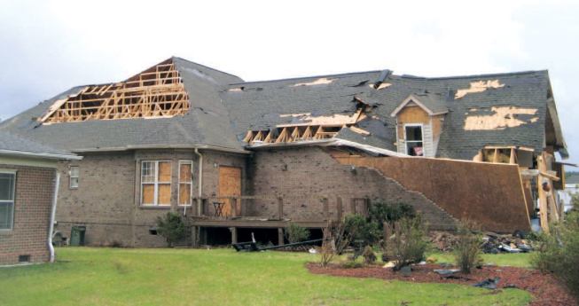 The same home, seen from the rear, also lost sheathing at the step-down trusses of the hip roof, a type of failure I observed several times. Top-chord nailing surfaces on step-down trusses do not neatly align with the roof sheathing, which makes it more difficult to attach the sheathing adequately.