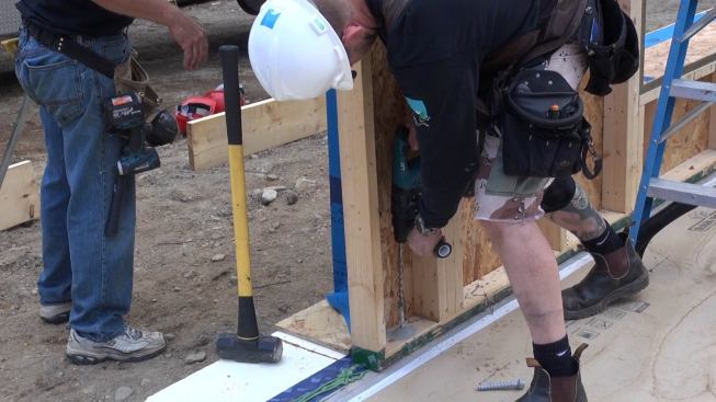 Corson drills a hole through the wall plate and into the slab with a hammer drill in preparation for setting an anchor bolt.