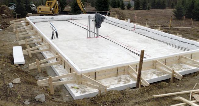 After the air-vapor barrier is installed, the interior is filled with compacted gravel that's contoured to form the thickened edge. Long screws pushed through the vertical foam hold it to the hardened concrete.