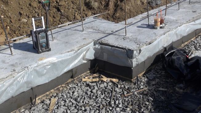 A view of the perimeter strip footings for the house’s basement foundation walls shows the layer-cake construction of the insulated footing detail: first, a base of compacted “trap rock,” then a layer of compacted crusher run, topped by a layer of sand, and then the insulating layer of Pittsburgh Corning Foamglas. Plastic slip sheeting above the Foamglas keeps the concrete footing isolated from the Foamglas, so that expansion or shrinkage of the concrete won’t damage the relatively brittle insulation material.