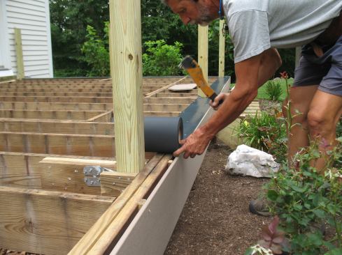 The old stained rim board is covered with Earthwood Evolutions fascia to dress up the perimeter of the deck. Flexible flashing covers the joint between the rim joist and the fascia, which is installed over blocking.