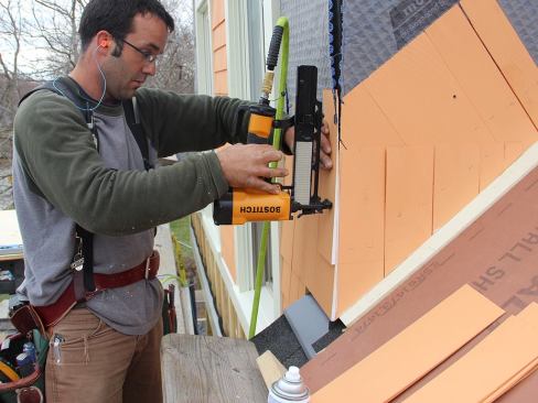 Pollard fastens a shingle after cutting the edge flush to match the corner. Note the with edge of the freshly cut shingle, where he primed the exposed wood with rattle-can spray primer.