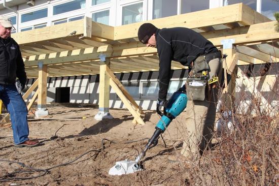 Pins are set almost flush to the concrete hub, using the depth of the driving bit on the jackhammer as a gauge. Fully driven pins project five feet into the ground in this case, but the pins for a larger unit with greater bearing capacity may go much farther down.
