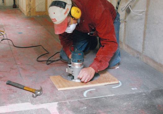 A worker uses a plywood jig to rout channels in the Wedi floor panels.