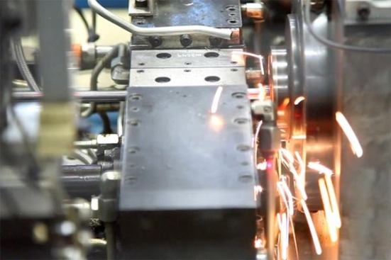 This machine is friction welding the socket end of a nut driver onto the hollow shaft. The shaft is being held in place by a clamp while the machine spins the socket against it fast enough and hard enough to melt the two pieces of metal together. The sparks are being produced by friction alone.