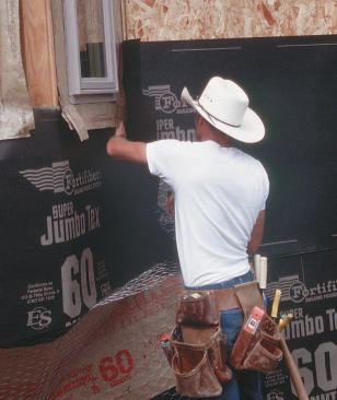 Integrating building papers with window flashings can be a challenge on site. In California, where this crew works, stucco contractors aren't typically licensed to install windows, so the paper crew must work with the existing flashing. Here, the window crew left the window perimeter protected by strips of flashing, with side strips lapped over the bottom strip and the head strip lapped over the side strips and the window flange. The paper installer lifts the bottom flap and runs paper under it.