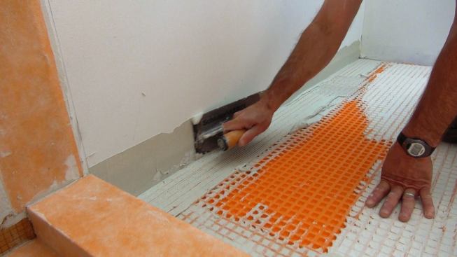 Boucher works mortar into the drywall and into the Ditra membrane at the floor-to-wall intersection.