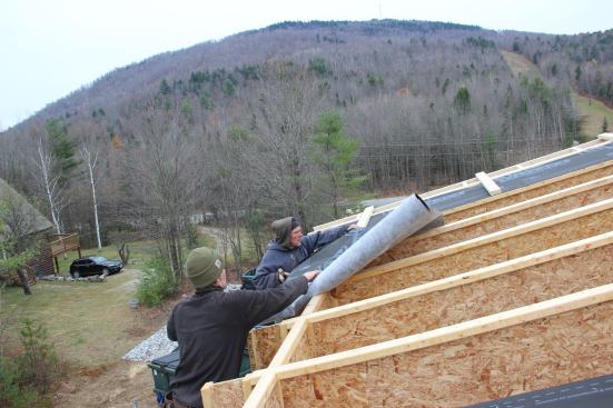 With gable overhangs already framed out on the lower shed-roof portion of the addition, Maine Passive House contractor Jesper Kruse and carpenter Todd place Pro Clima Mento Plus fabric at the roof eave.